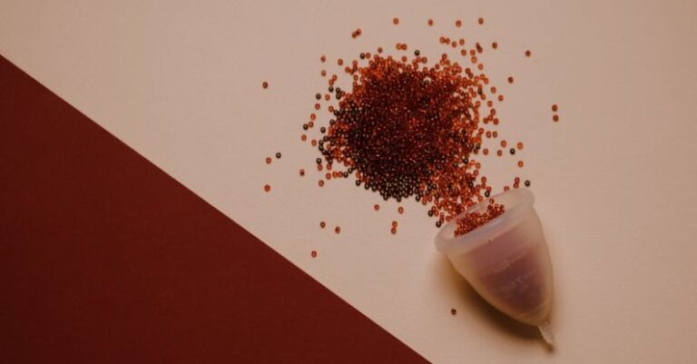 Bleed - Top view of silicone menstrual cup with red beads scattered on pink surface