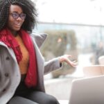 Video Content - Happy excited African American female laughing and gesticulating while having video calling on laptop and sitting at modern cafe