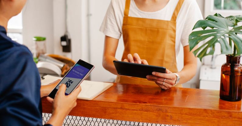 QR Codes - Crop anonymous female employee with application on cellphone screen interacting with partner using tablet at counter in cafeteria