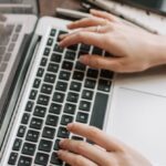 Digital Flipbooks - From above of unrecognizable woman sitting at table and typing on keyboard of computer during remote work in modern workspace